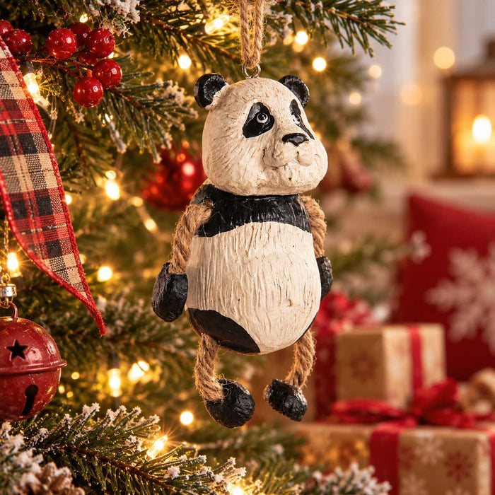 A carved panda tree ornament hanging from a Christmas tree with warm string lights, red ornaments, and wrapped gifts in the background.